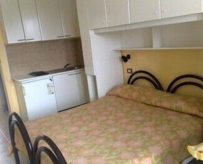 A small room with a bed, a desk, and a kitchenette. - Residence Nettuno (Campomarino)