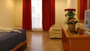 Quarto de hotel com cama, cadeira, escrivaninha e televisão.