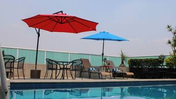Zona de piscina con sillones de descanso y dos sombrillas, una roja y otra azul.