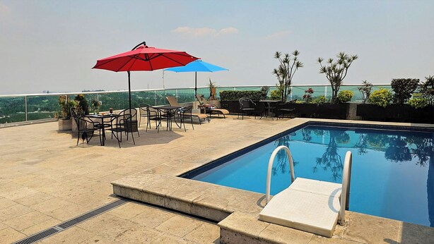 Uma área de piscina no terraço com vista ampla do horizonte da cidade, piscina com trampolim e área de estar externa com guarda-sóis.