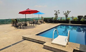 A rooftop pool area with a clear view of the city skyline, a pool with a diving board, and outdoor seating with umbrellas. - Hotel GS Cuernavaca (Cuernavaca)