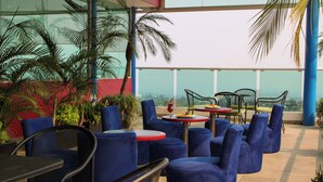 Terraço no telhado com assentos acolchoados em azul, mesas vermelhas e amarelas, e plantas em vasos.