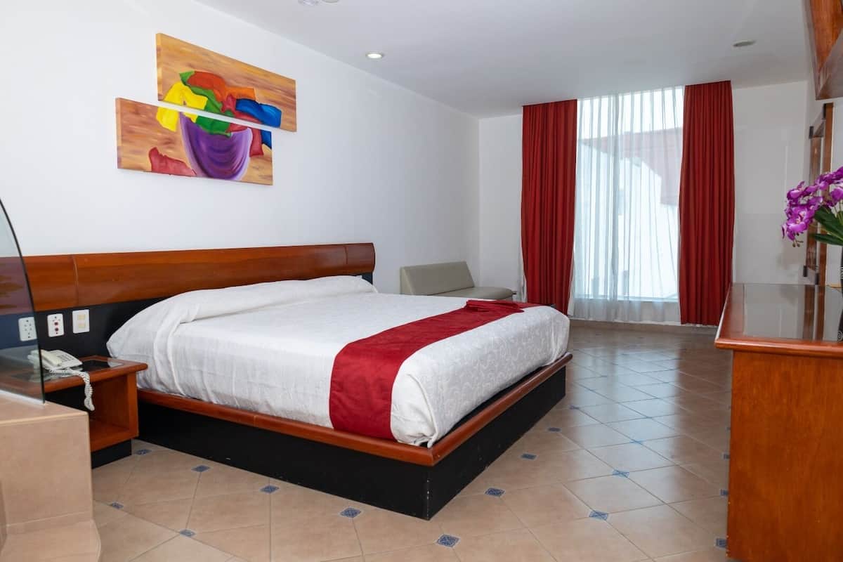 Une chambre d’hôtel avec un lit, un bureau, un téléphone et un tableau au mur.