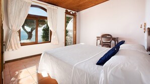 Un dormitorio con una cama grande, techo de madera, ventana con cortinas y vista a árboles.