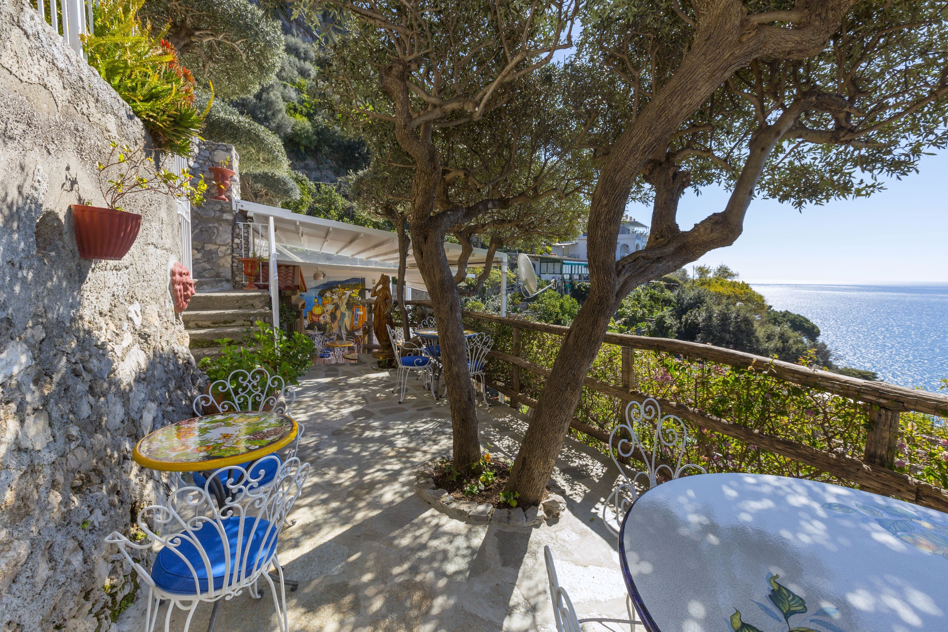 A terrace with outdoor seating, a stone wall, and a view of the sea.