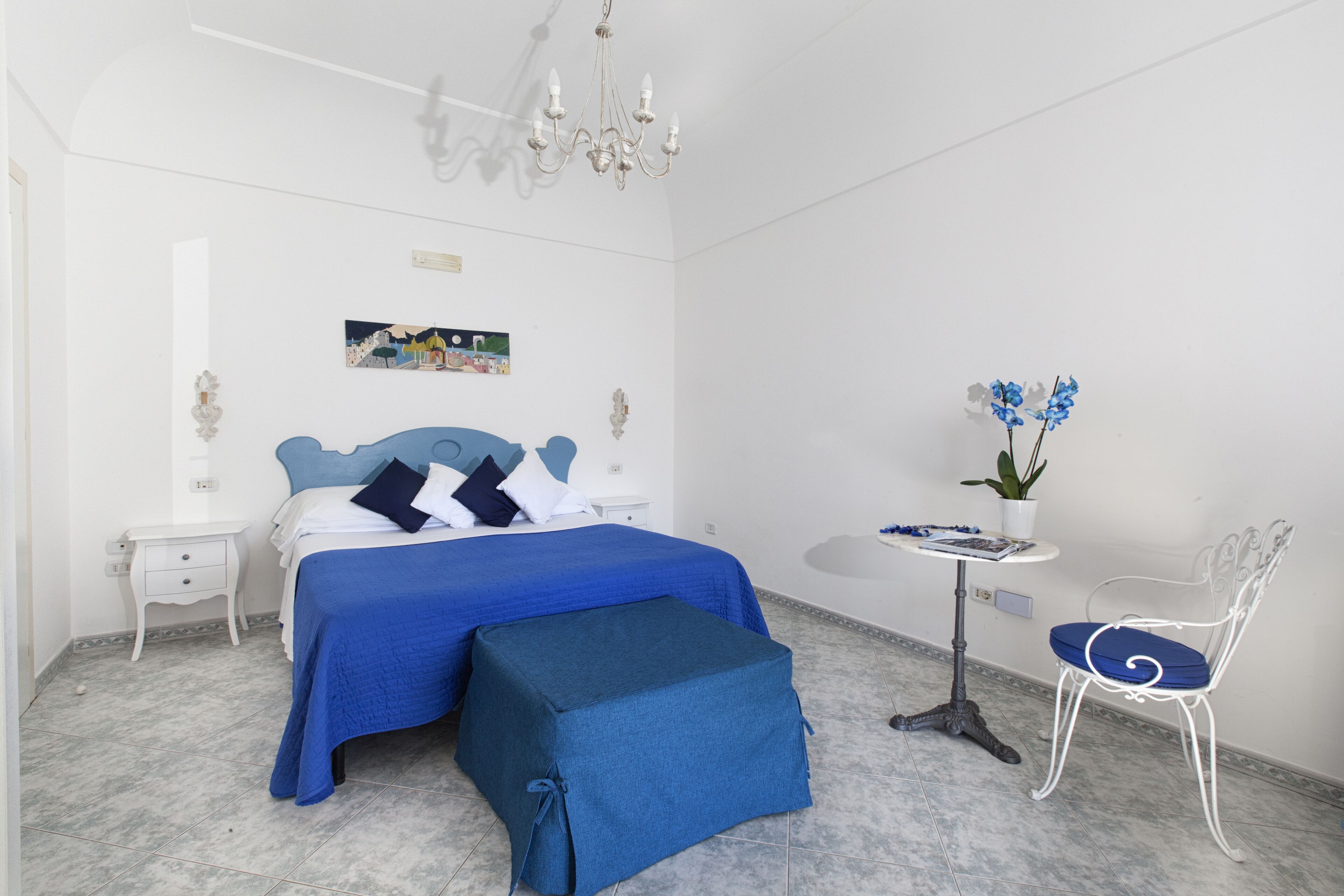 Une chambre à coucher avec un lit, une table de chevet, une petite table avec une plante, une chaise et un lustre.