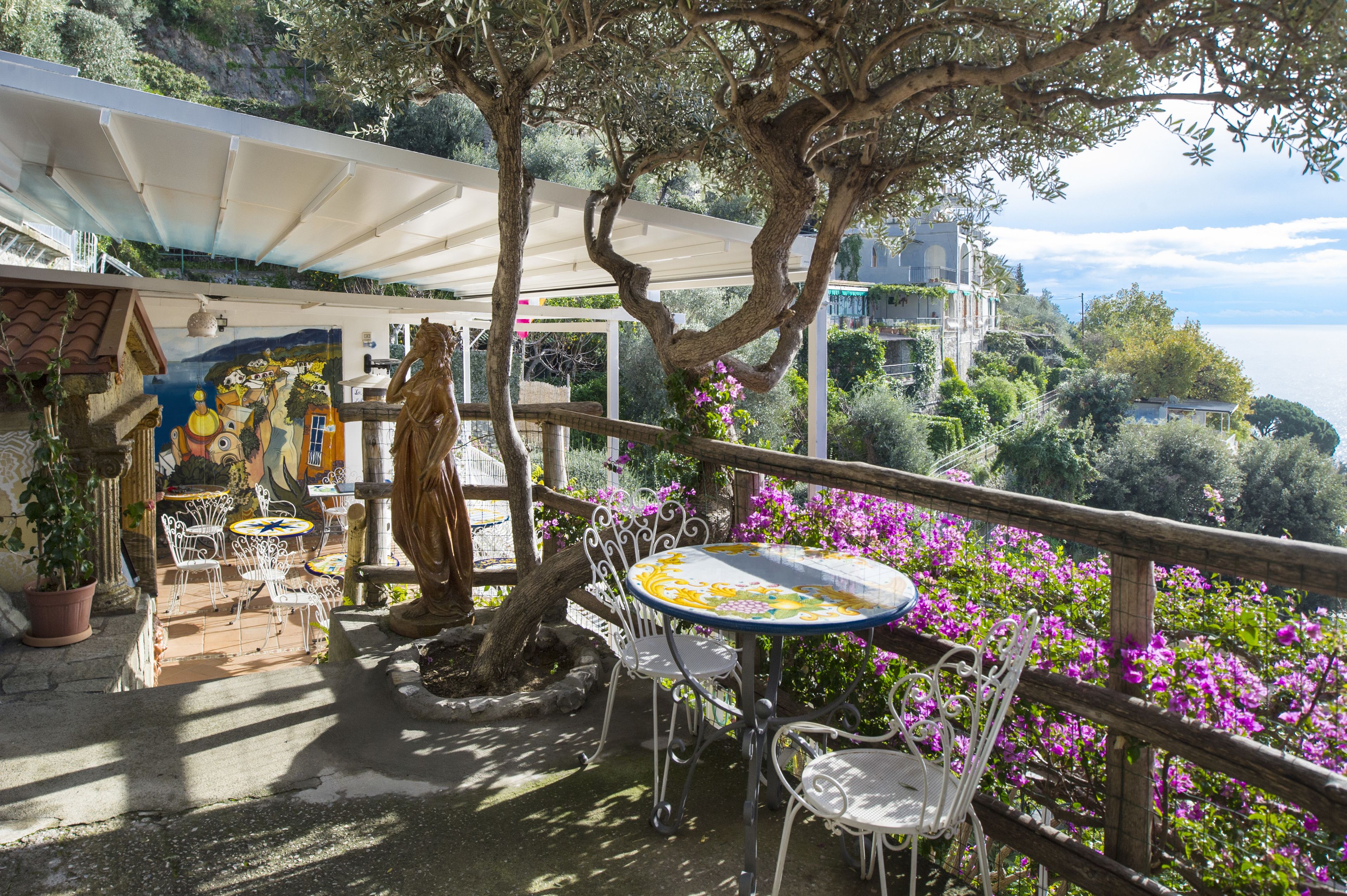 An outdoor patio with a table and chairs, surrounded by potted plants and a mural.