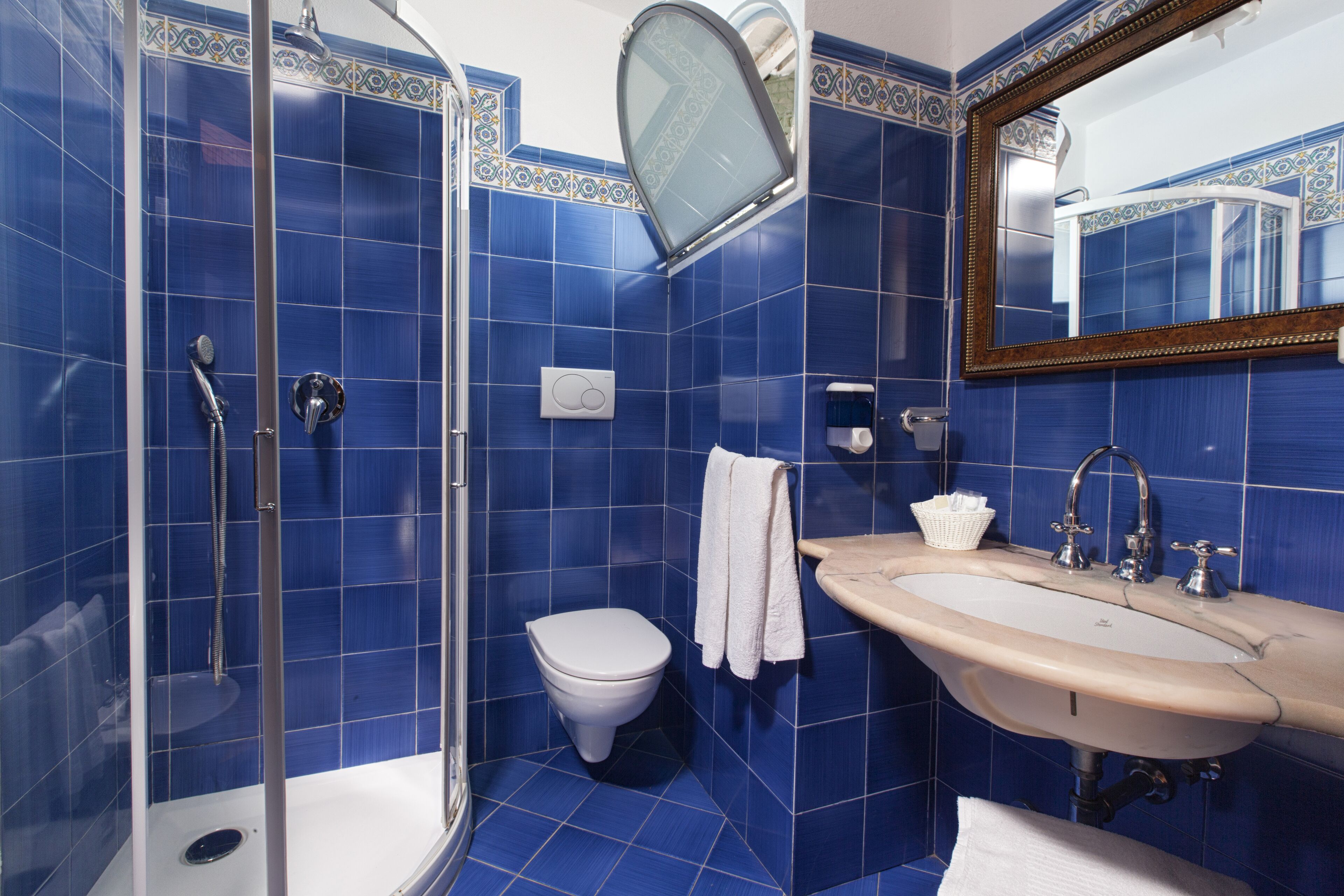 A bathroom with blue tiles, a white toilet, a shower, a sink, and a mirror.