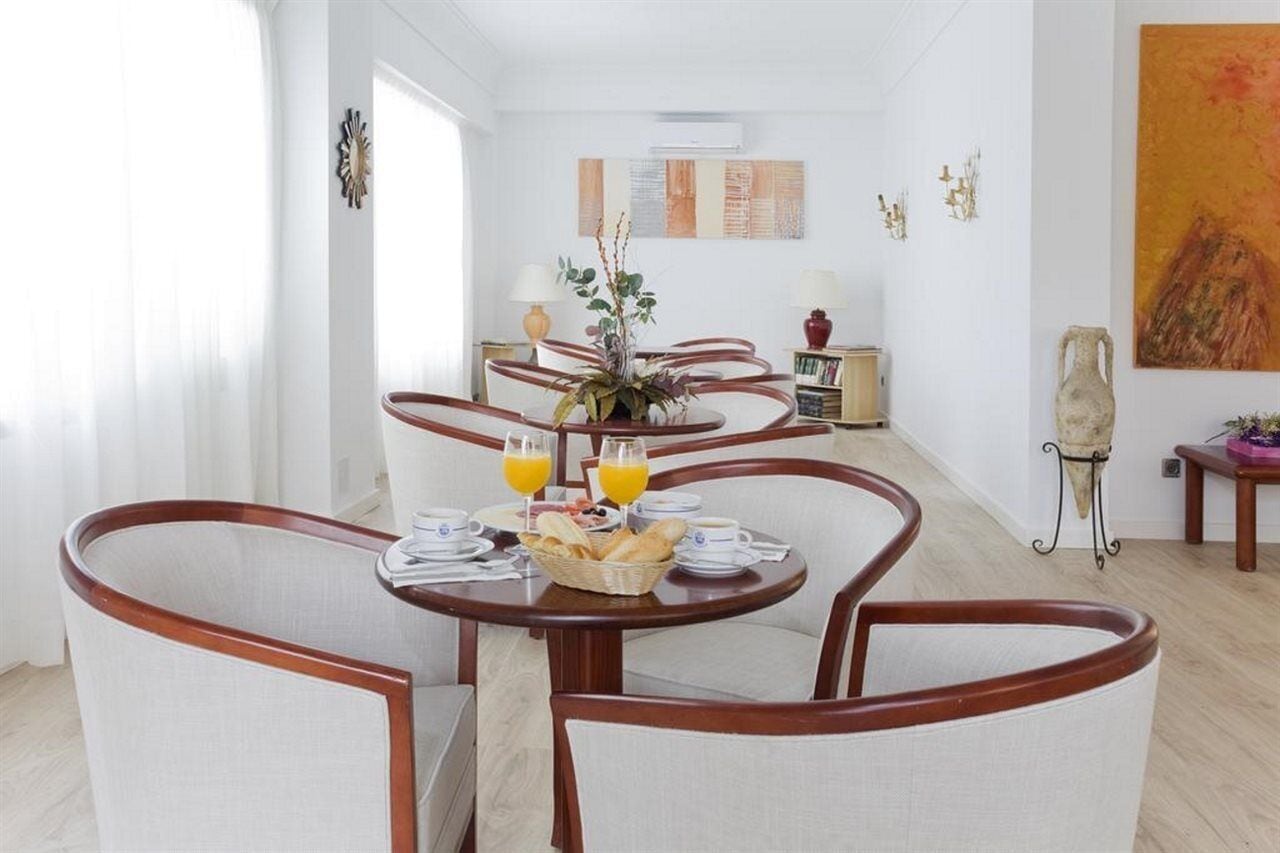 Un comedor con una mesa redonda dispuesta para el desayuno, que incluye pan, bollería y zumo de naranja.