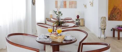 Un comedor con una mesa redonda dispuesta para el desayuno, que incluye pan, bollería y zumo de naranja.