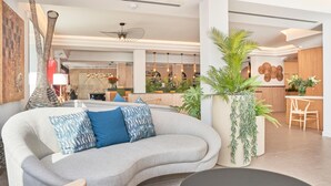A modern living room with a grey sofa, blue cushions, a large potted plant, and a black coffee table. - Flacalco Hotel & Apartments (Capdepera)