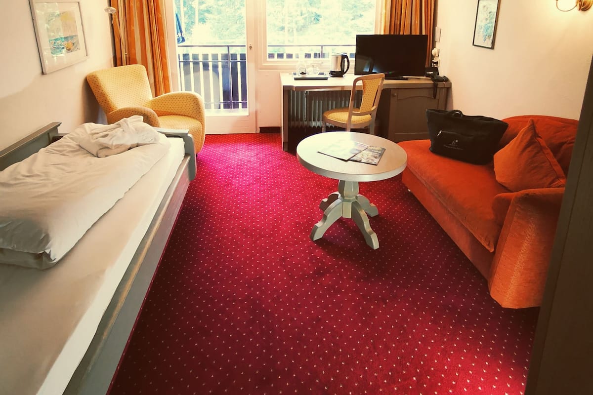 A hotel room with a bed, a sofa, a small table, a TV, and a window with curtains.