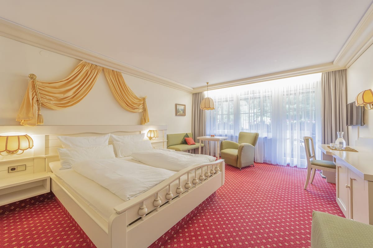 A hotel room with a large bed, a desk, a chair, and a small table.