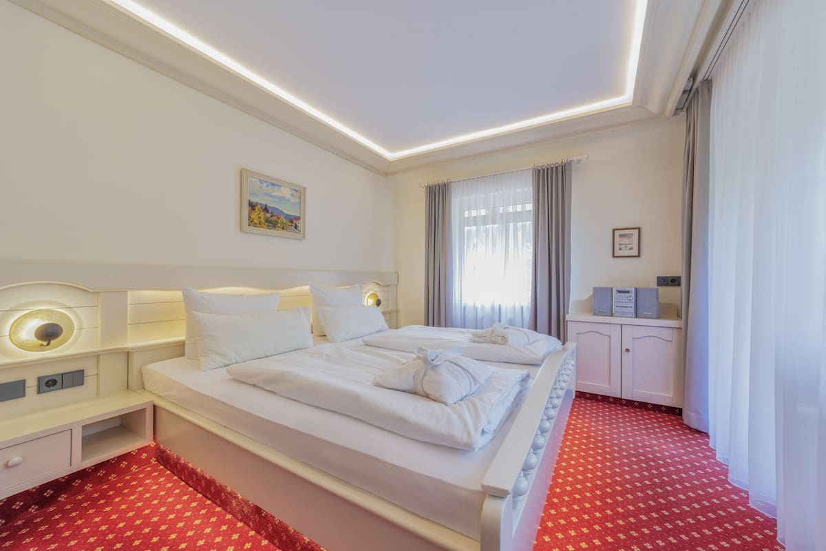 A hotel room with a large bed, bedside tables, a small cabinet, and a red patterned carpet.