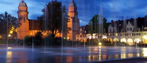 A historic building with two towers and a fountain in front.