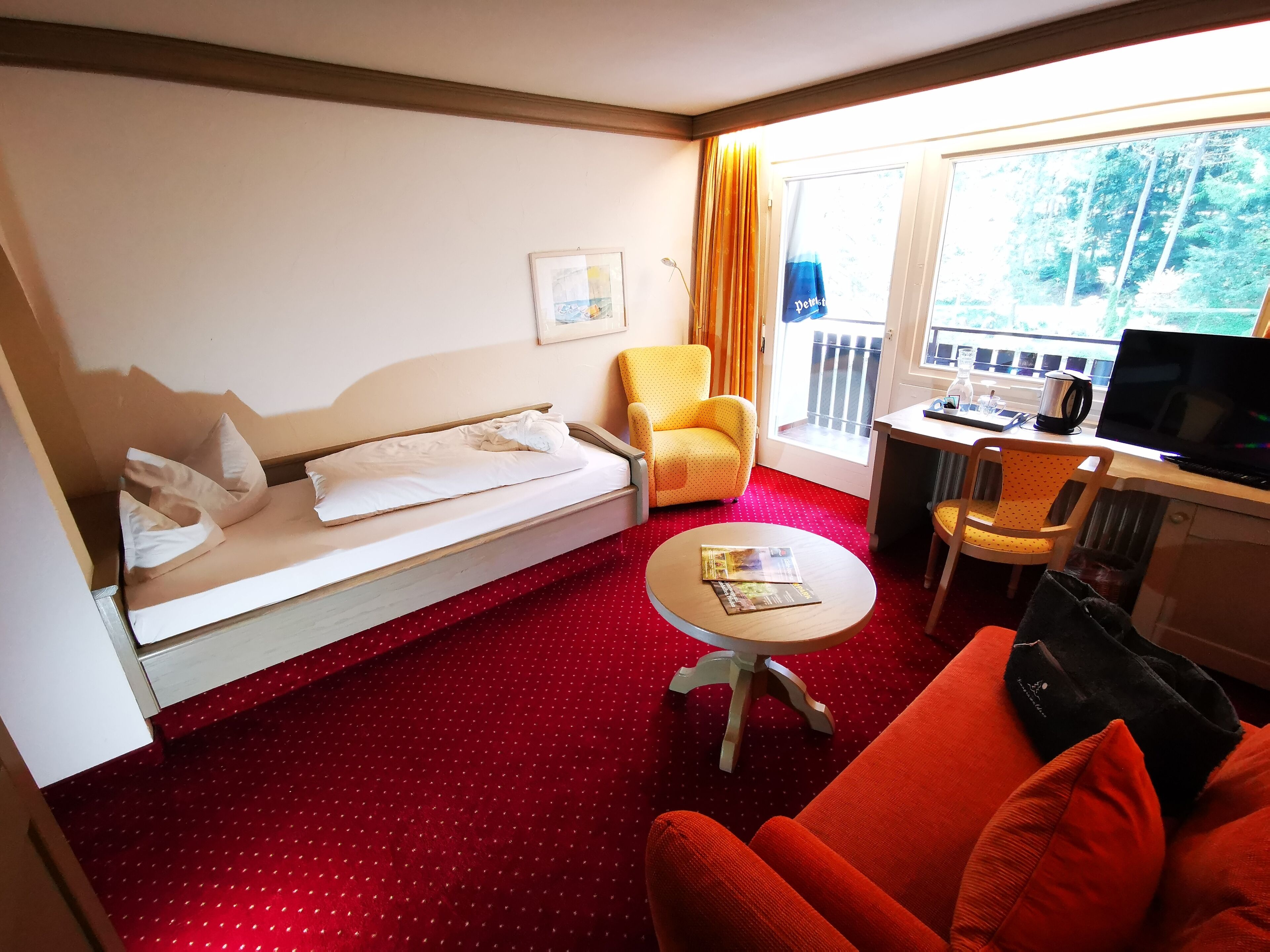 A hotel room with a bed, a sofa, a small table, a desk with a laptop, and a window with curtains.