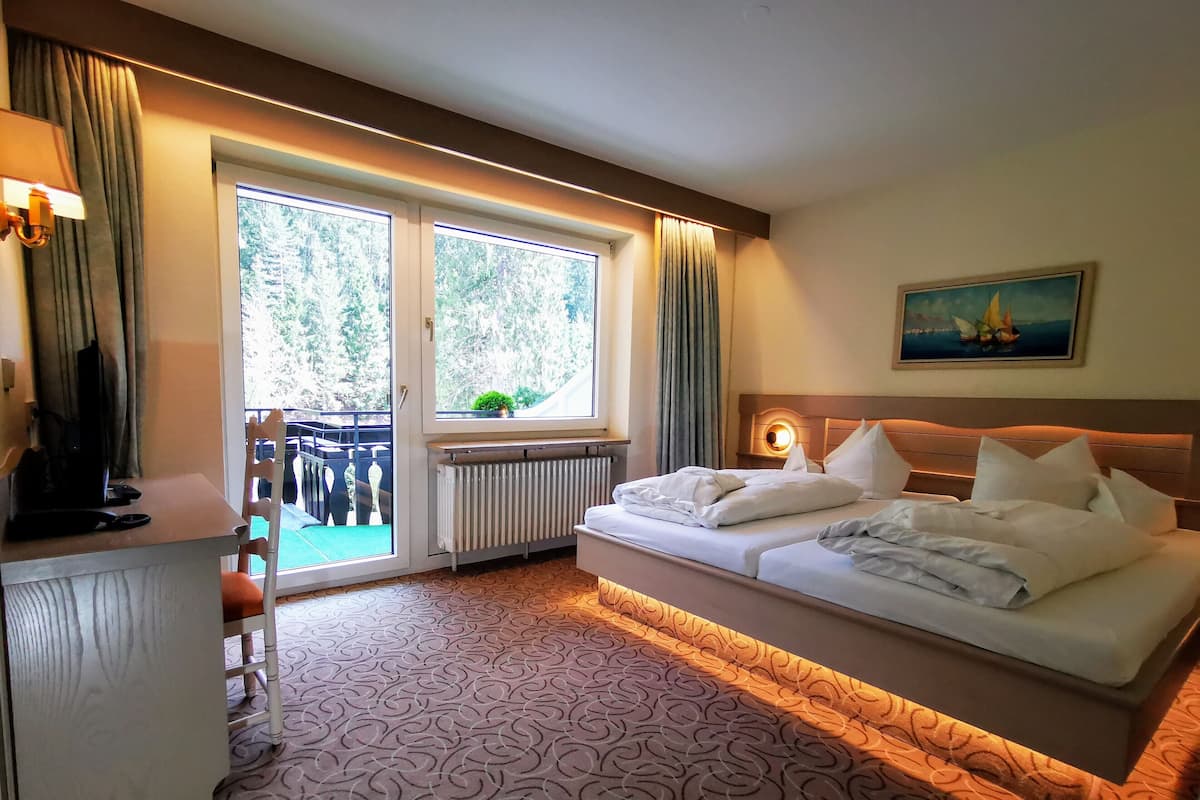 A hotel room with a bed, a desk, a chair, a radiator, and a view of the outdoors.