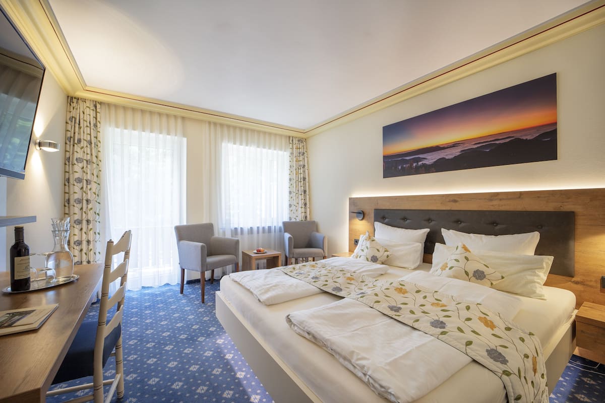 A hotel room with a large bed, two armchairs, a small table, and a TV.