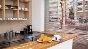 A modern kitchen with a wooden countertop, a coffee machine, and a view through large windows. - Hotel Parisien (Menton)