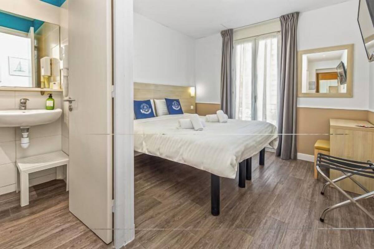 A hotel room with a bed, a bedside table, a chair, a sink, and a mirror.