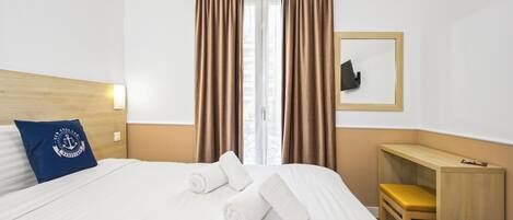 A hotel room with a bed, a wooden headboard, a desk, a chair, a mirror, and curtains.