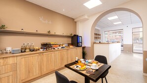 A breakfast area with a wooden counter, a coffee machine, and a table set for two with plates of food. - Hotel Parisien (Menton)