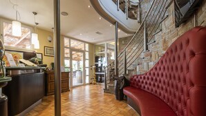 A spacious lobby with a curved staircase, a red leather sofa, and a reception desk. - Agriturismo Corte Benedetto (Capannori)