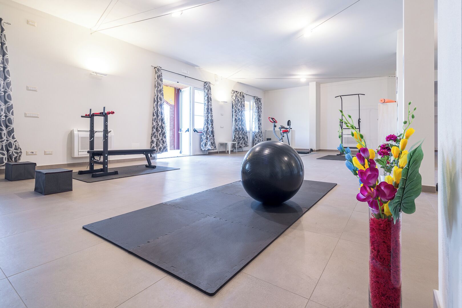 Una habitación amplia con una pelota grande de ejercicios, una banca y un soporte para pesas.