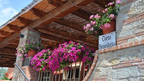 A stone building with a wooden pergola and hanging flower baskets. - Agriturismo Corte Benedetto (Capannori)