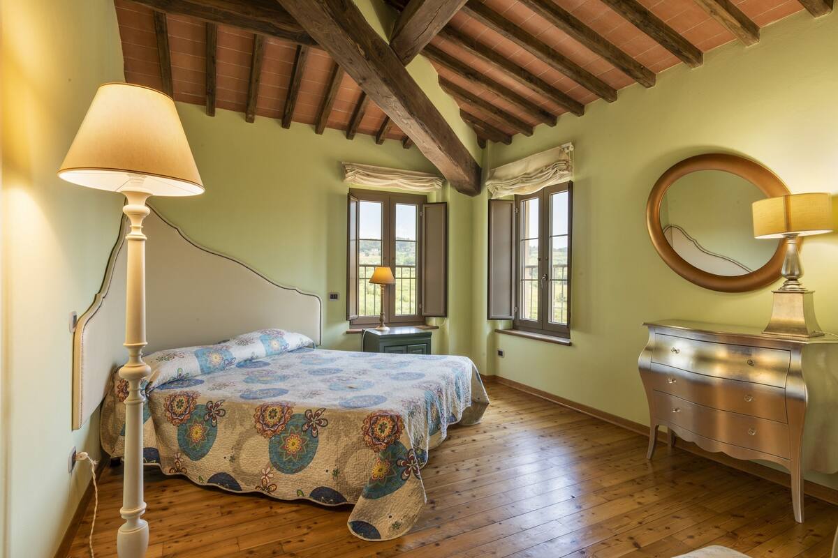 Una camera da letto con soffitto in legno, un letto con copripiumino fantasia, un comò e uno specchio.