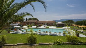 A pool area with lounge chairs and umbrellas, surrounded by greenery and a building with a tiled roof. - Agriturismo Corte Benedetto (Capannori)