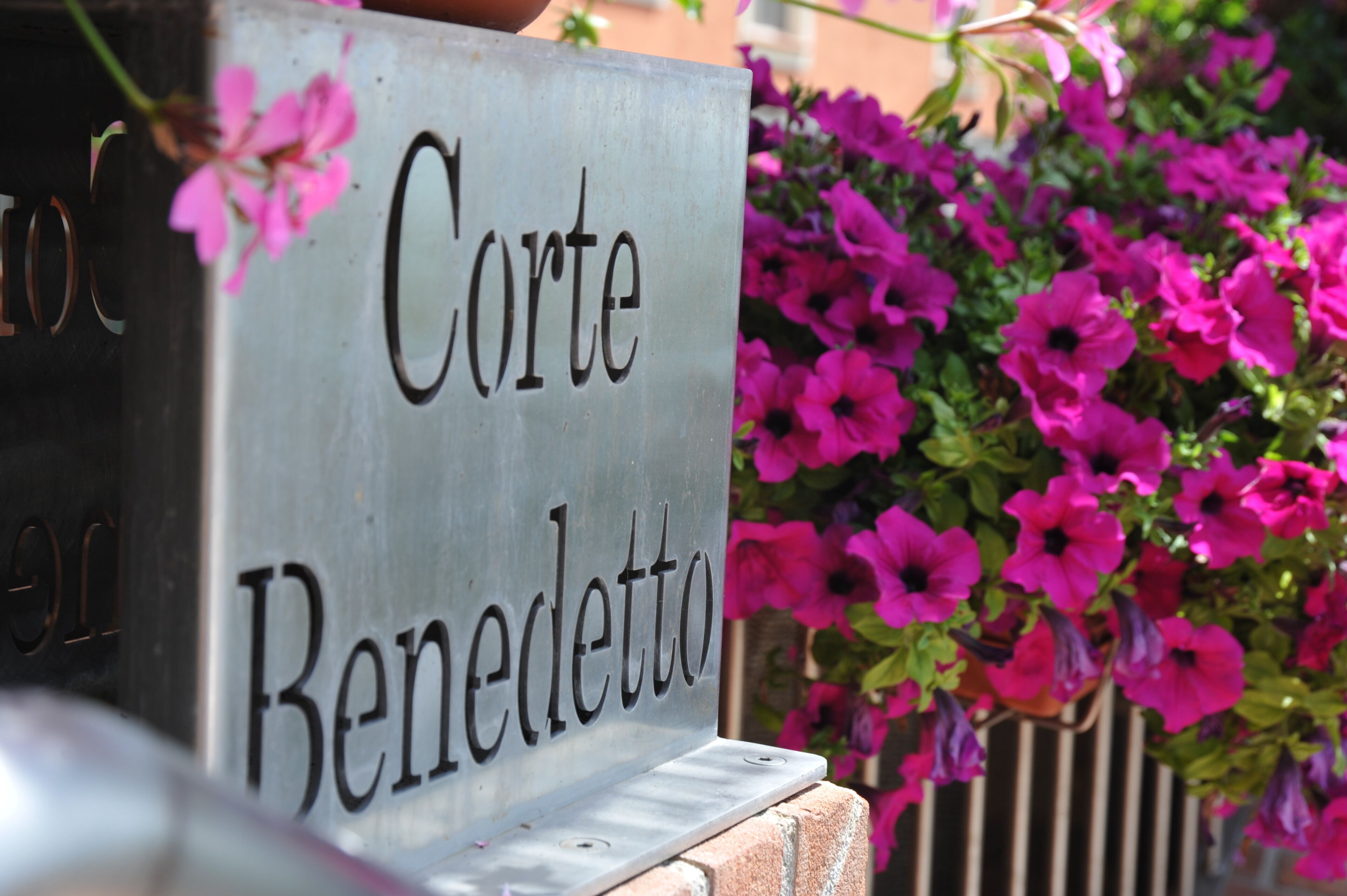 A metal sign with the name 'Corte Benedetto' mounted on a brick structure.