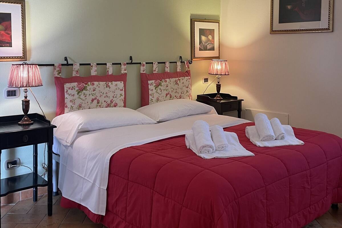 Una camera d'albergo con un letto matrimoniale, due comodini, una lampada e due quadri appesi al muro.