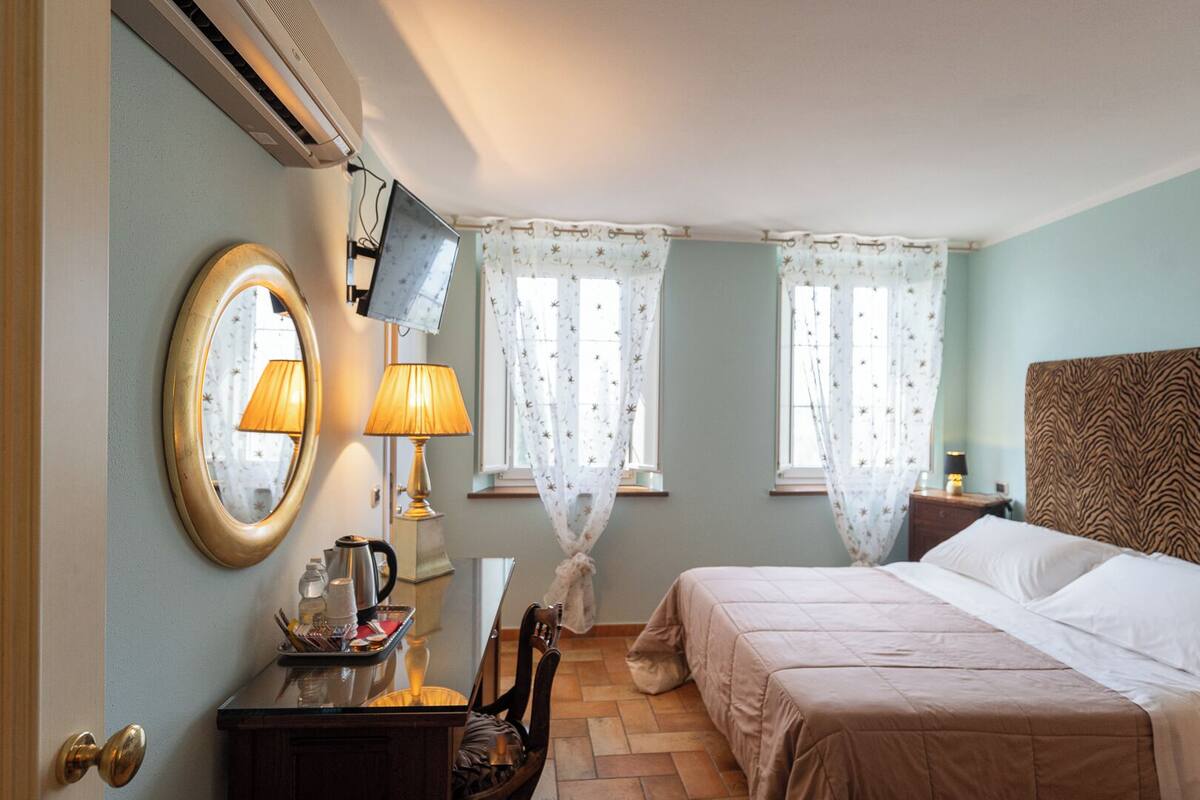Camera d'albergo con un letto, una scrivania con una lampada, uno specchio e una TV appesa al muro.
