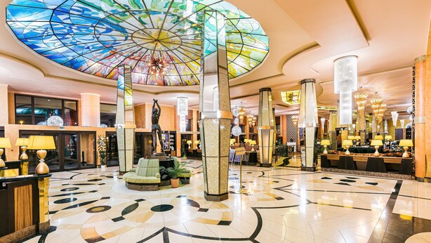 A lobby with a large stained glass ceiling, a reception desk, seating area, and a check-in counter.