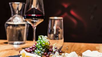 A charcuterie board with various cheeses, fruits, and nuts on a slate board, accompanied by wine glasses and a pitcher.