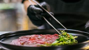 A chef preparing a dish with a black plate, a red sauce, and green garnish.