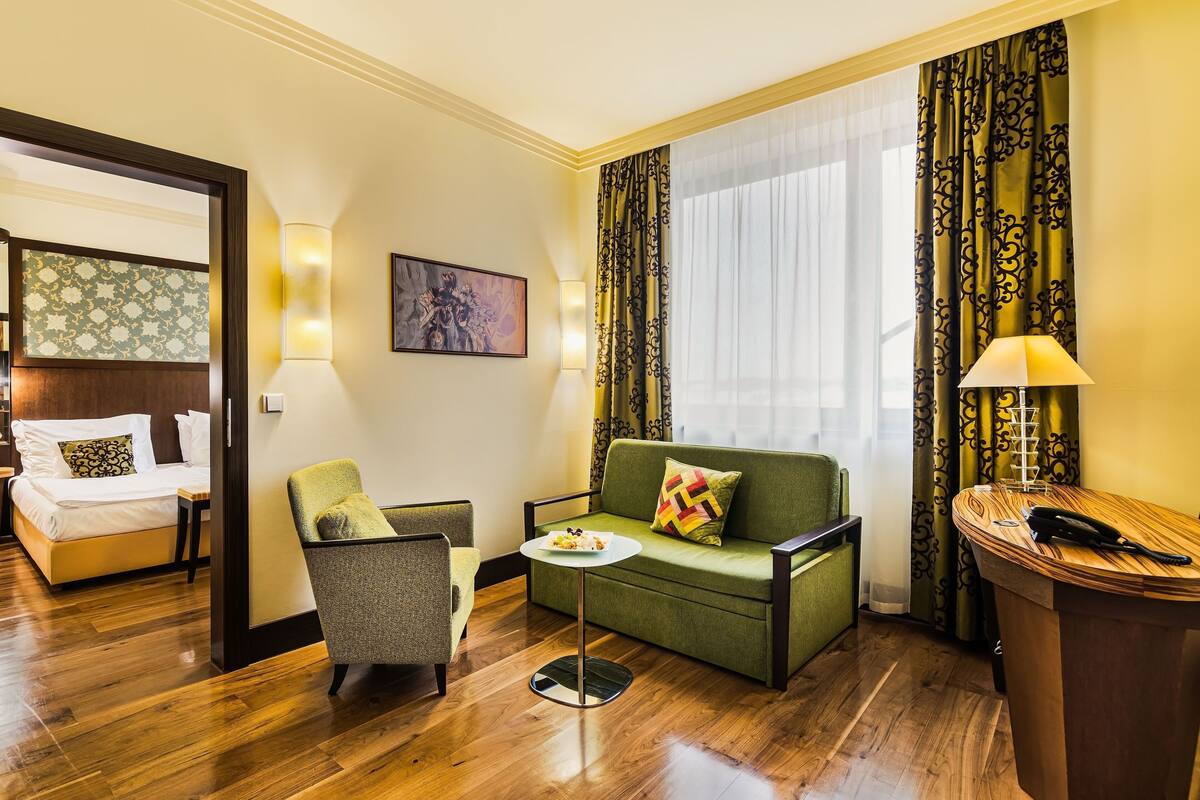 A hotel room with a bed, a sofa, a chair, a small table, and a desk with a lamp.
