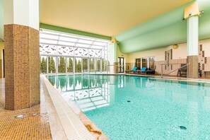 Una amplia piscina cubierta con paredes de vidrio transparente, suelo de baldosas y vistas a árboles fuera.