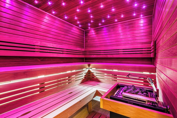 A sauna with wooden benches and pink lighting.