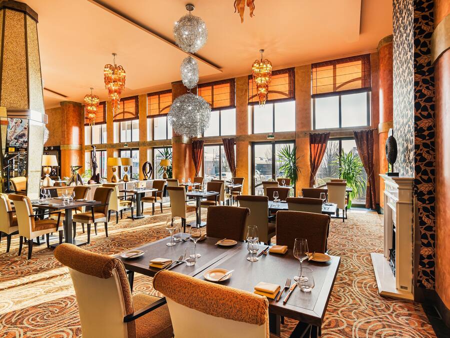 A spacious dining area with multiple tables and chairs, large windows, and decorative chandeliers.