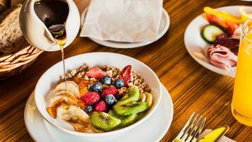 A breakfast setting with a bowl of fruit and granola, a glass of orange juice, and a bottle of honey being poured.