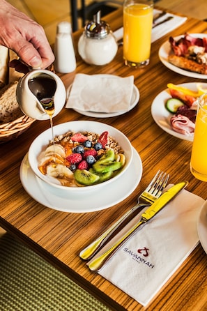 Desayuno con un tazón de fruta y granola, un vaso de jugo de naranja y una botella de miel siendo servida.