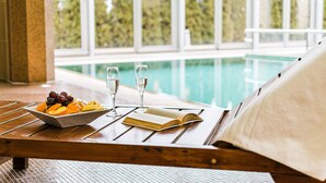 A poolside lounge with a table set with fruit, glasses, and a book, overlooking a swimming pool.