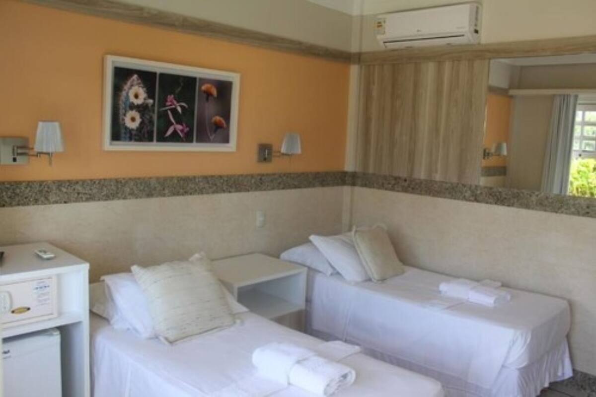 Habitación de hotel con dos camas, un escritorio, un refrigerador pequeño y un aire acondicionado instalado en la pared.