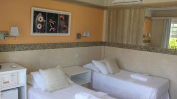 A hotel room with two beds, a desk, a small fridge, and a wall-mounted air conditioner.