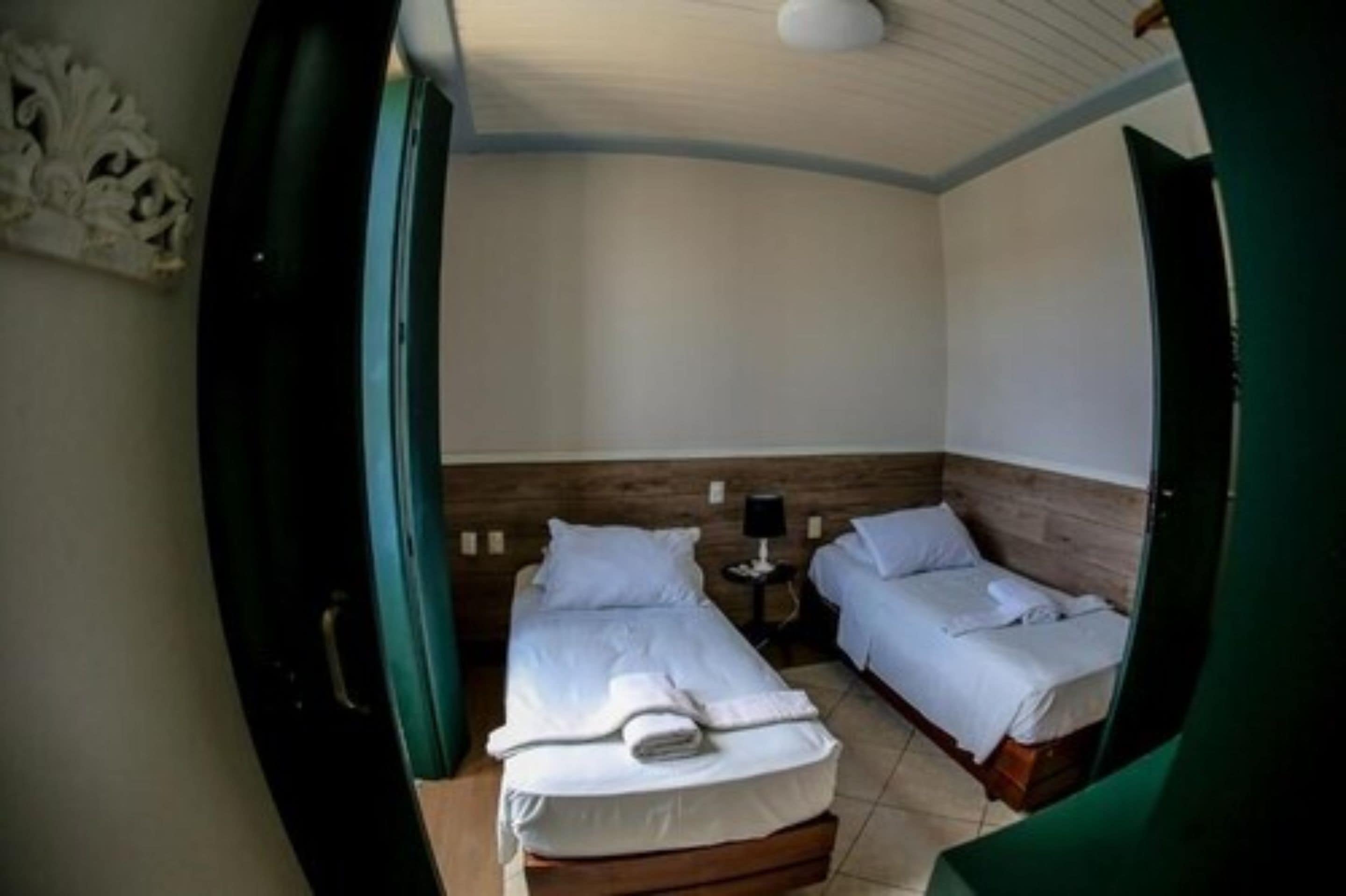 A room with two beds, a small table with a lamp, and a wooden headboard.