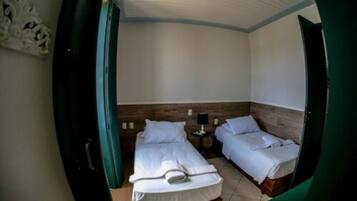 A room with two beds, a small table with a lamp, and a wooden headboard.