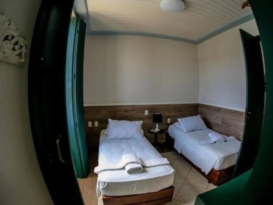 A room with two beds, a small table with a lamp, and a wooden headboard.