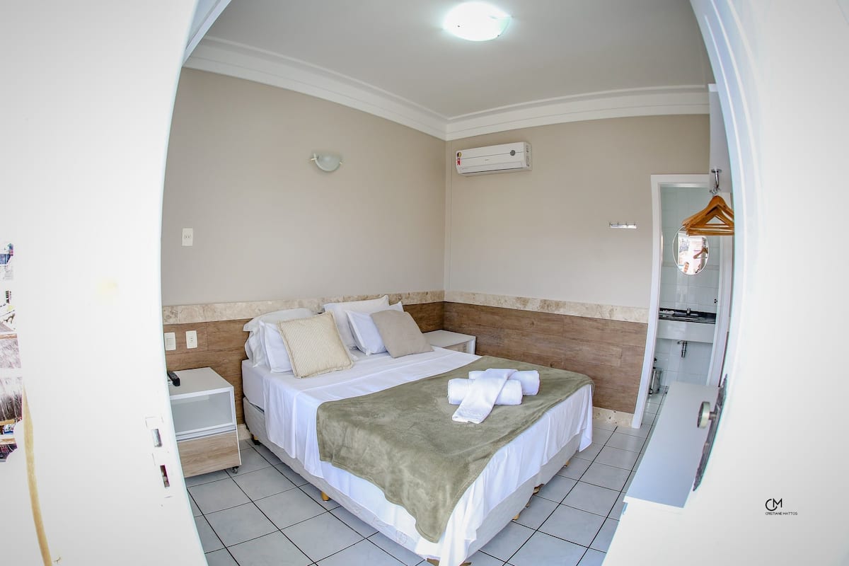 Una cama bien hecha con un edredón verde, una mesita de noche y un aire acondicionado de pared.